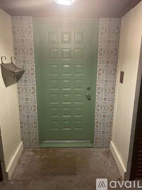 A green door with a wallpapered wall behind it.