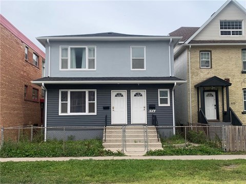 A grey house with a white door and a black railing.
