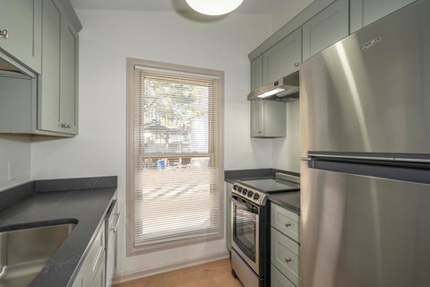 A kitchen with a stainless steel refrigerator and a window with blinds.