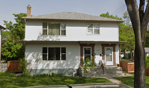 A white house with a grey roof and a brown door.