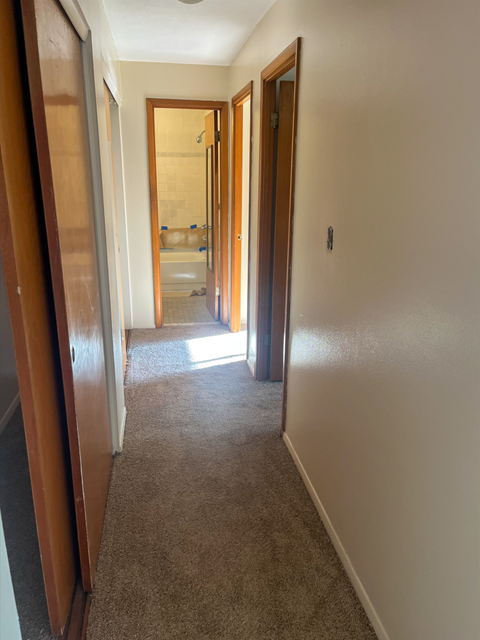 A hallway with a carpeted floor and white walls.