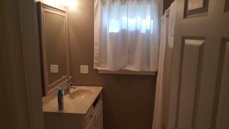 A bathroom with a sink, mirror, and a window with curtains.