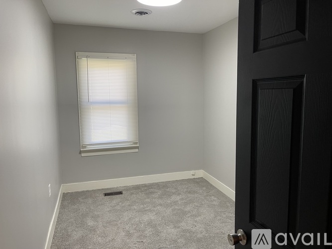 A room with a carpeted floor, a window with blinds, and a door.