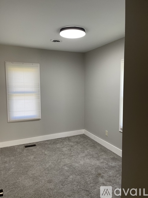 A room with a carpeted floor, a window with blinds, and a ceiling light.