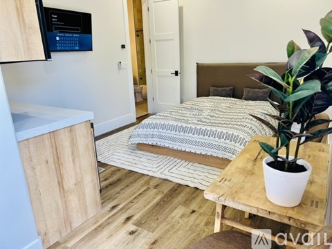 A bedroom with a bed, a plant, and a TV mounted on the wall.