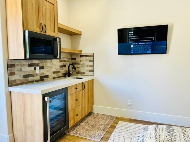A kitchen with a microwave, oven, and a TV mounted on the wall.