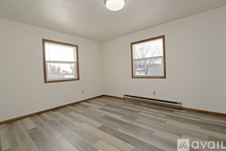 A room with wooden flooring and two windows.