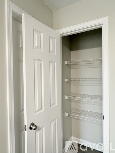 A white door with a handle is open to a white pantry with shelves.