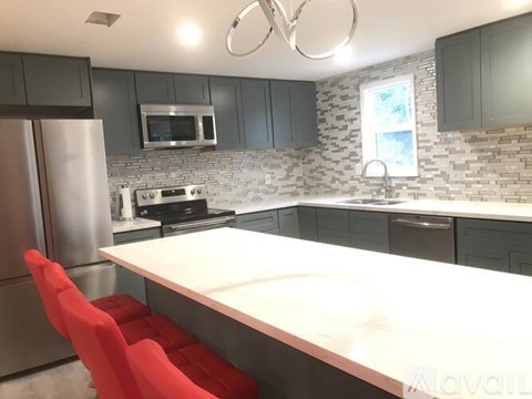 A kitchen with a long white table and red chairs.