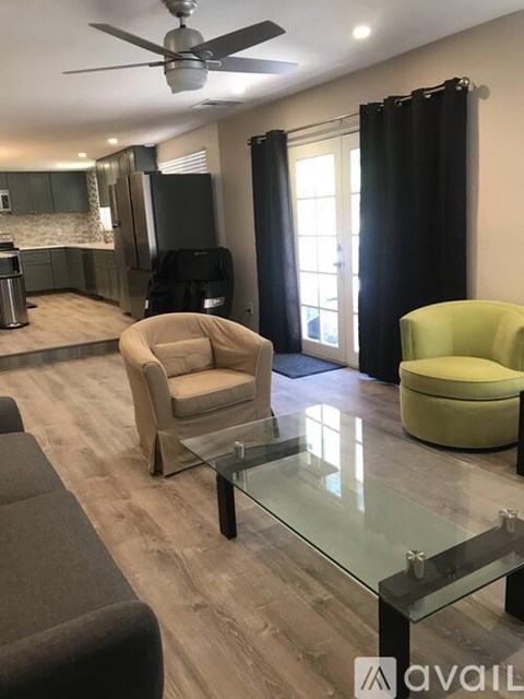 A living room with a glass table and a fan on the ceiling.