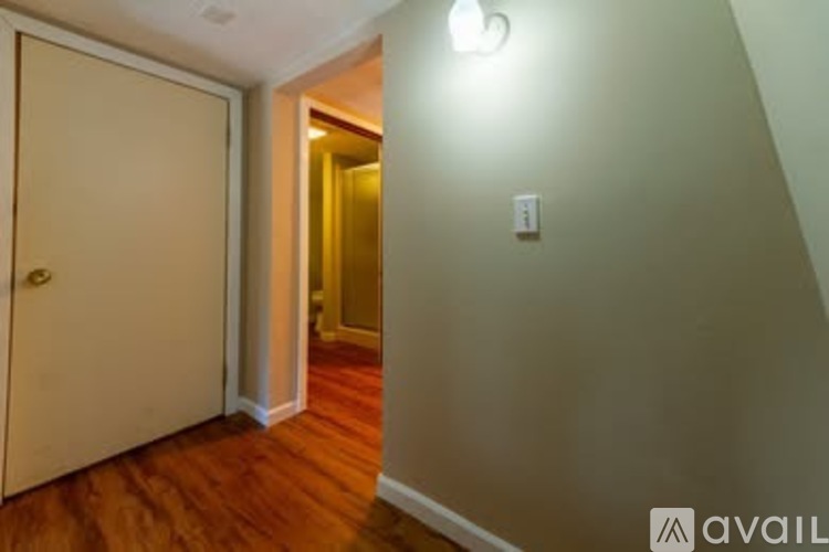 A hallway with a door on the left and a light switch on the wall.