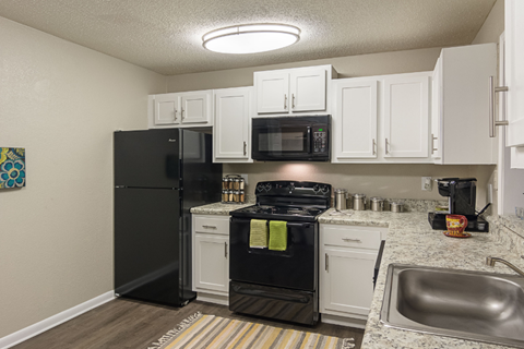 A black refrigerator and oven in a kitchen with white cabinets.