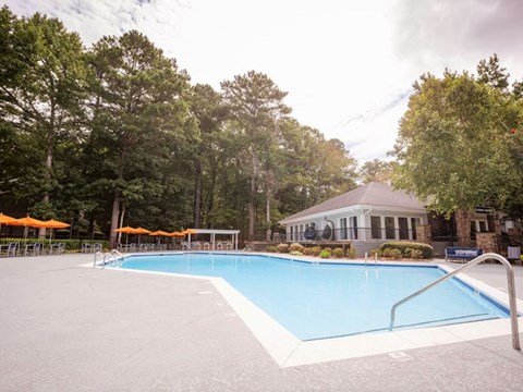 A large swimming pool surrounded by trees and a building in the background.