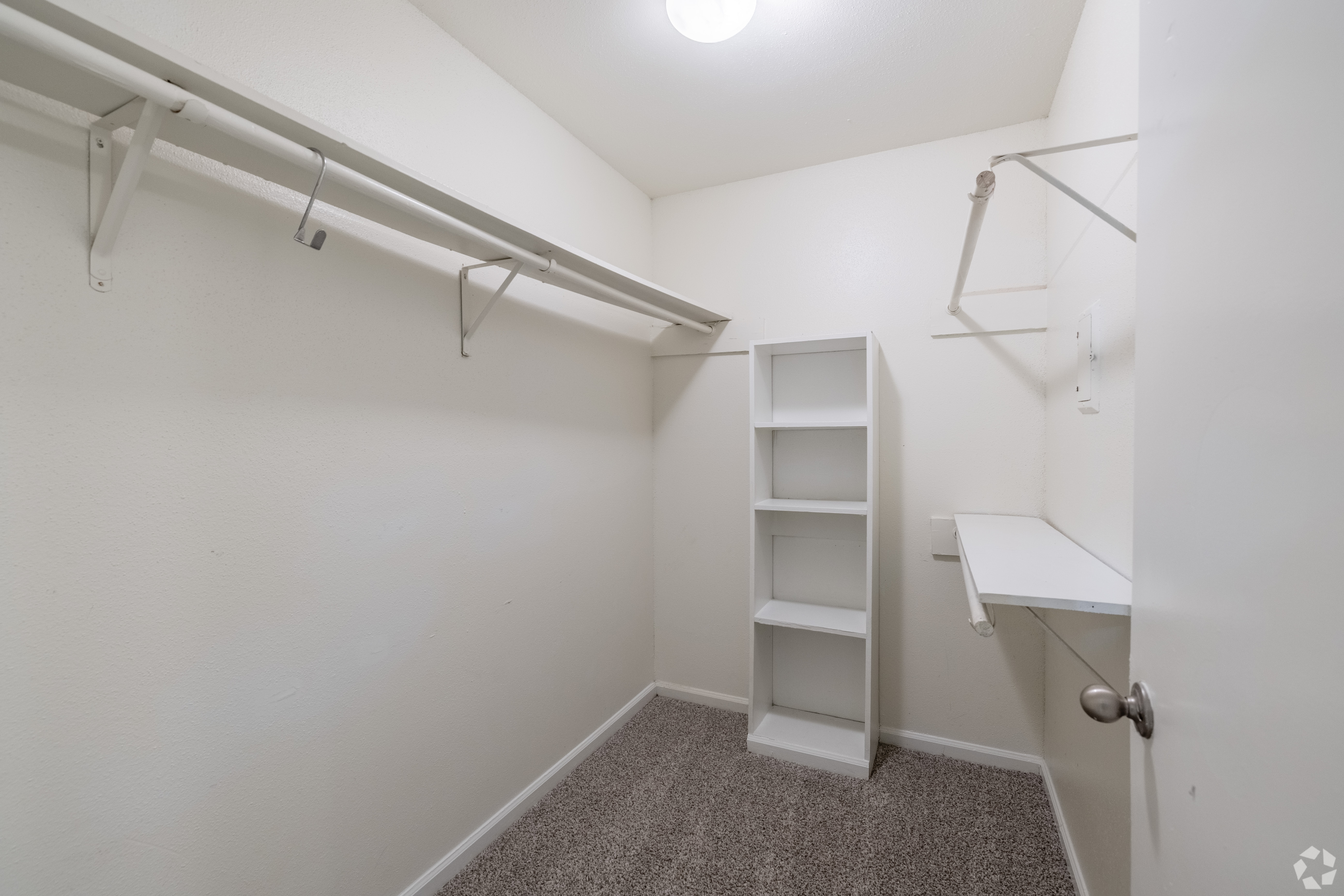 A small white closet with a shelf and a door.