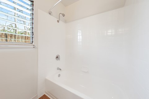 A white bathroom with a window and a bathtub.