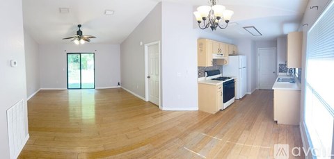 A spacious living room with a ceiling fan and a kitchen area with wooden floors.