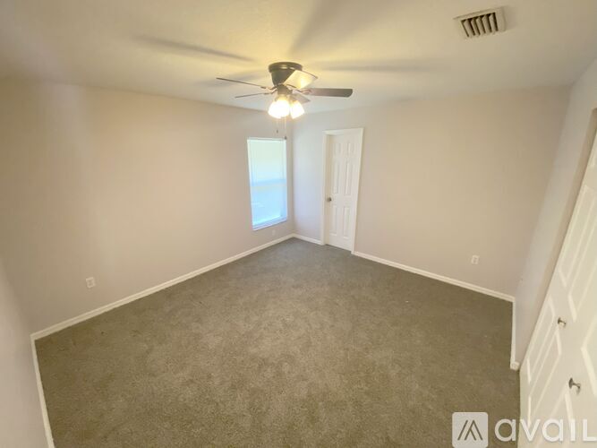 A room with a carpeted floor, a ceiling fan, and a door leading to a hallway.