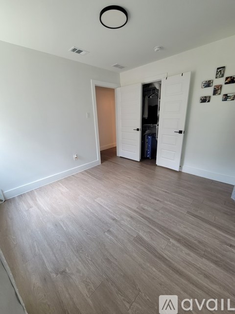 A room with wooden flooring and a white wall with a doorway leading to another room.