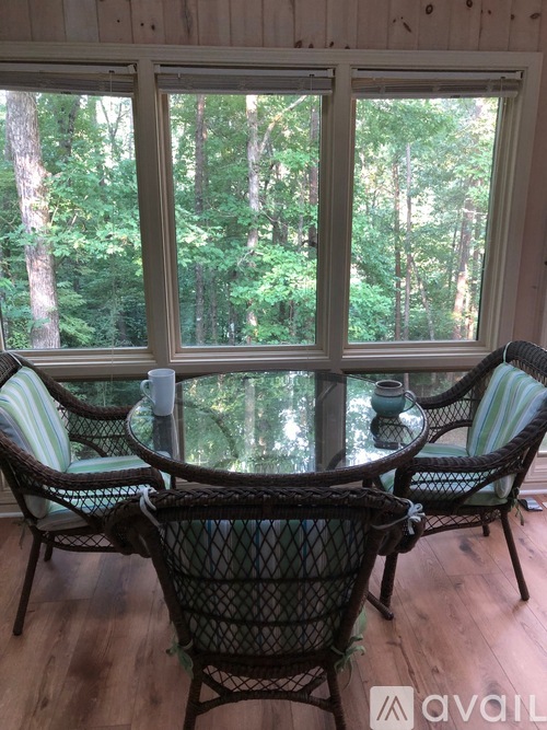 A table with chairs in front of a window with a view of trees.