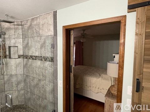 A bathroom with a walk-in shower and a bedroom with a bed and a nightstand.