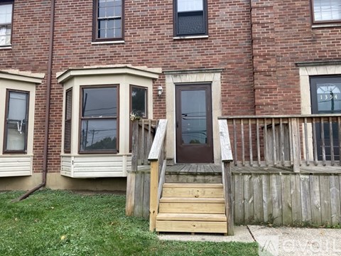 A house with a brown door and a wooden staircase leading to it.