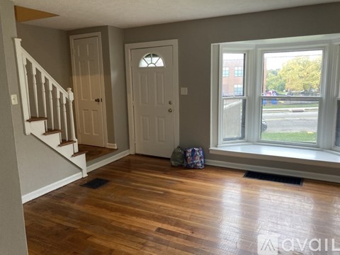 A room with a wooden floor, a staircase, and a door.