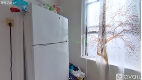 A white fridge in a room with a window showing a tree.