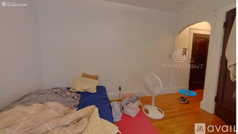 A room with a bed, a fan, and a red mat on the floor.