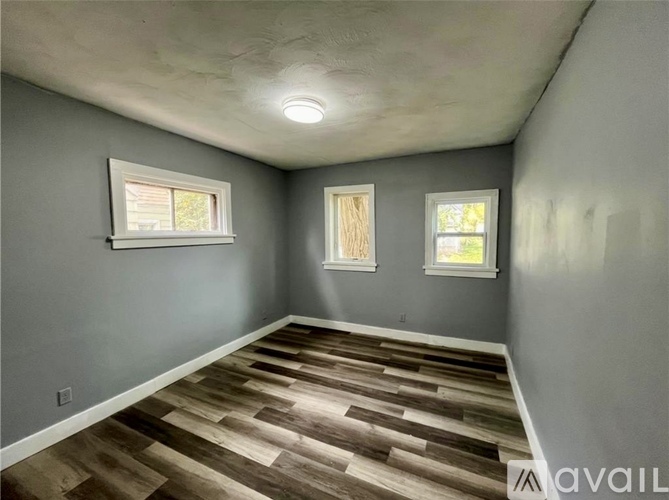 A room with wooden flooring and three windows.