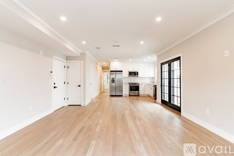 A spacious living room with hardwood floors and a kitchen area in the background.