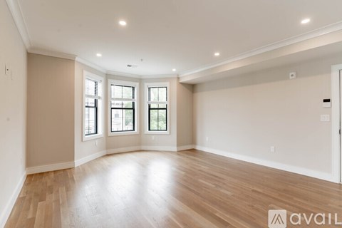 A spacious room with wooden flooring and three windows.