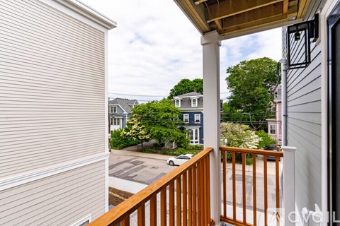 A view from a balcony looking out at a street with houses and trees.