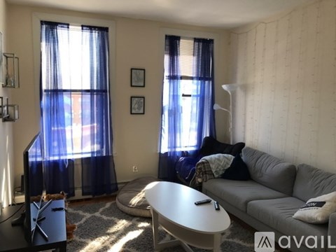A living room with a grey couch, a white table, and a window with blue curtains.