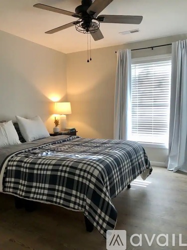 A bedroom with a bed covered in a plaid comforter and a ceiling fan above it.