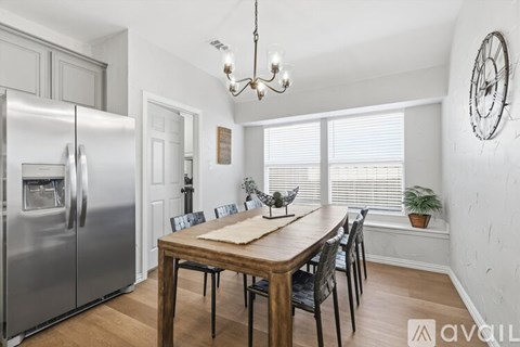 A kitchen with a wooden table and chairs, a refrigerator, and a chandelier.