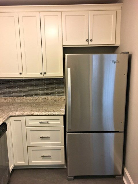 A stainless steel refrigerator stands in a kitchen with white cabinets.