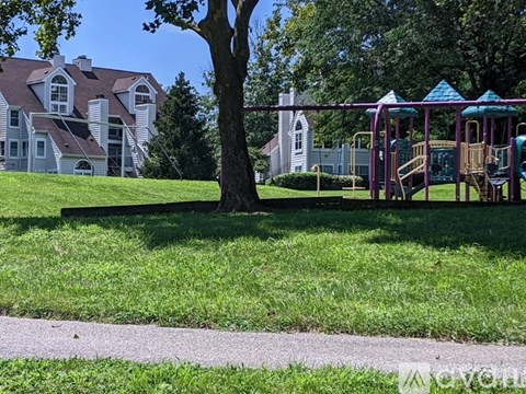 A playground with a swing set and a tree in front of a large house.