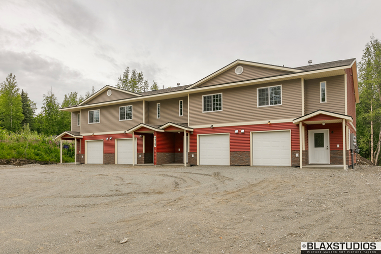 A two-story house with a garage is situated in a dirt lot.