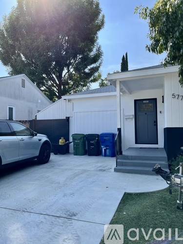 A white car is parked in front of a house with the number 577 on it.