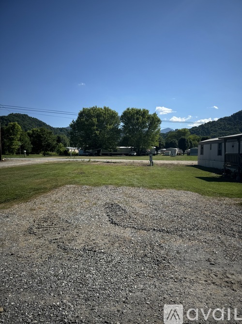 A gravel area in the foreground with a grassy field and buildings in the background.