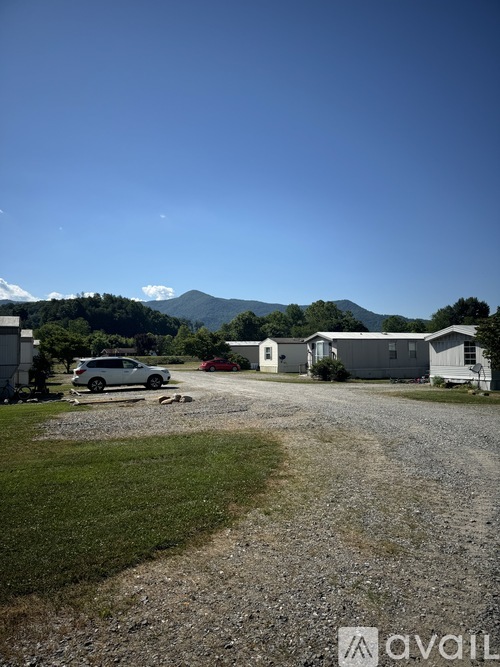 A gravel driveway leads to a house with a mountain in the background.