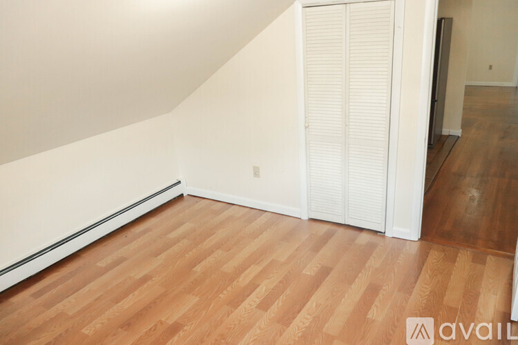 A room with wooden flooring and a white wall with a white door.
