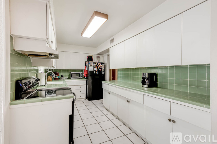 A kitchen with white cabinets and green tiles.