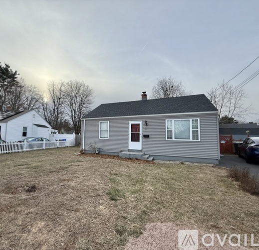 A house with a grey siding and a red door is surrounded by a white picket fence.