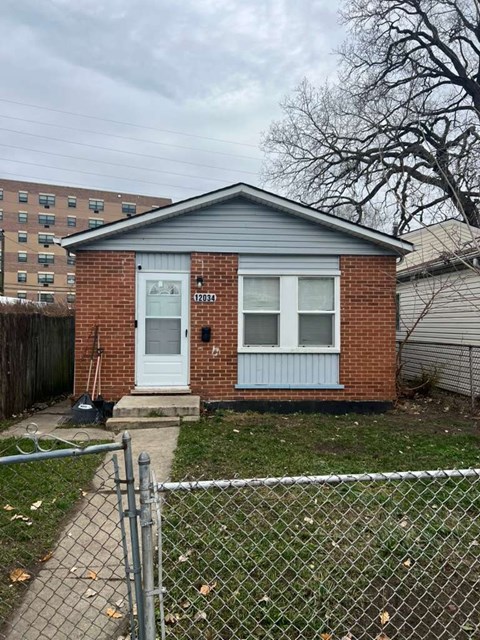 A small house with a white door and windows is surrounded by a chain link fence.