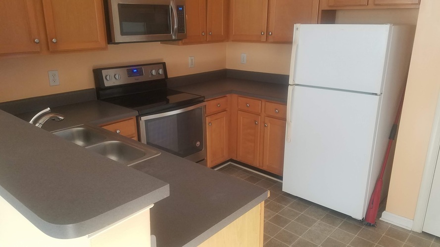 A white refrigerator stands in a kitchen with wooden cabinets.