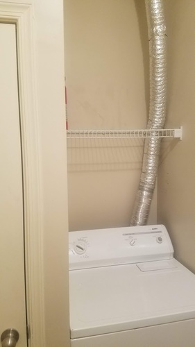 A white dryer is on a shelf in a bathroom.