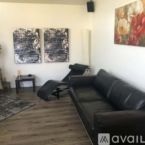 A black leather couch sits in a living room with a rug and two paintings on the wall.