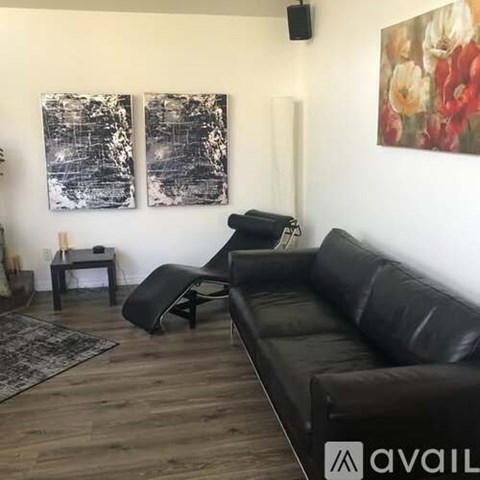 A black leather couch sits in a living room with a rug and two paintings on the wall.