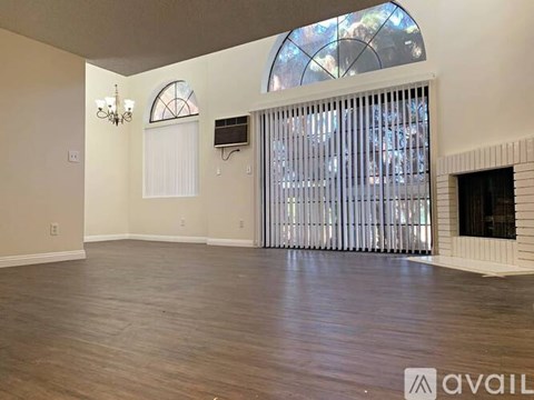 A spacious room with wooden floors and a large window with blinds.